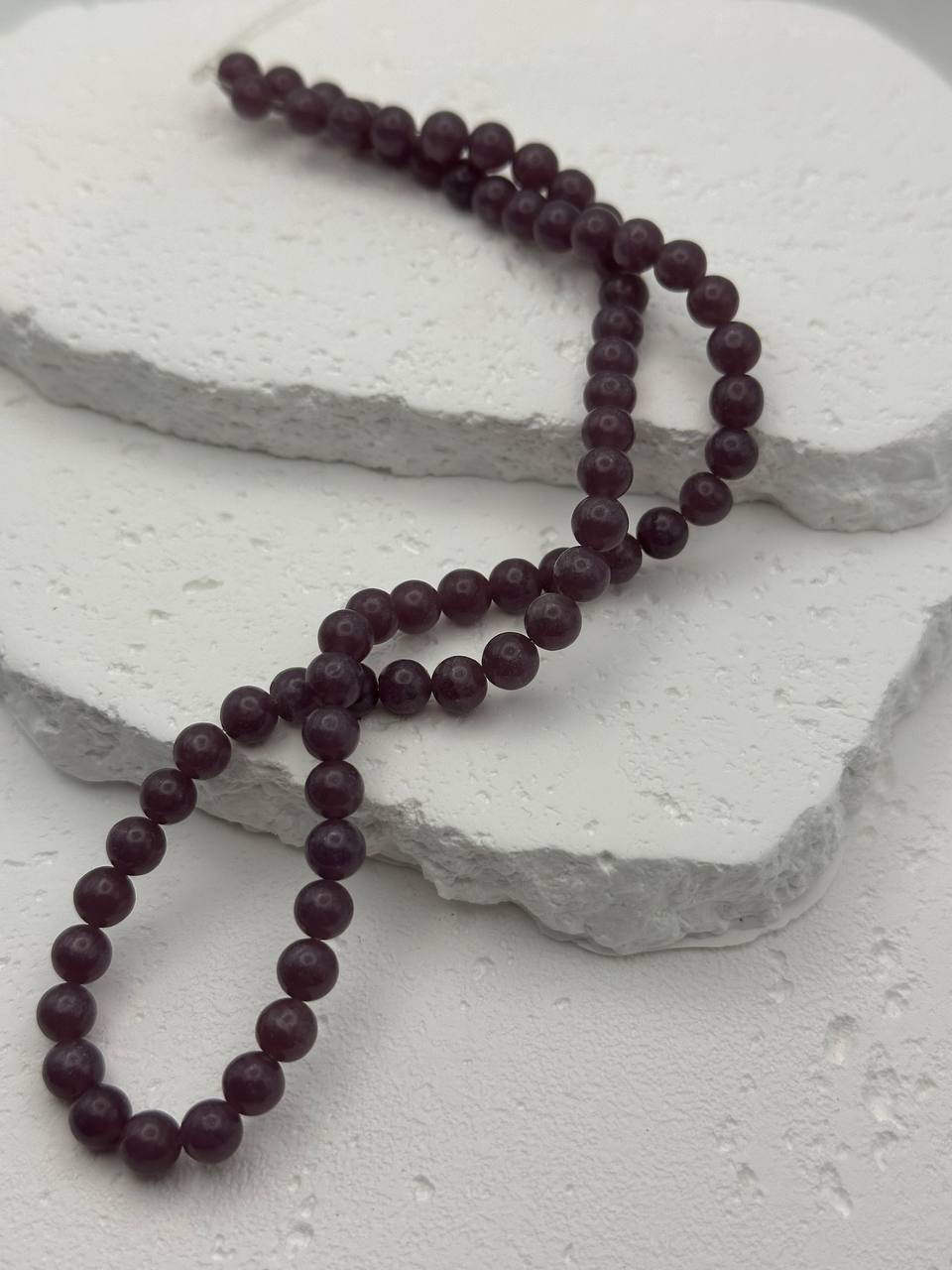 Dark purple lepidolite beads on a light stone surface