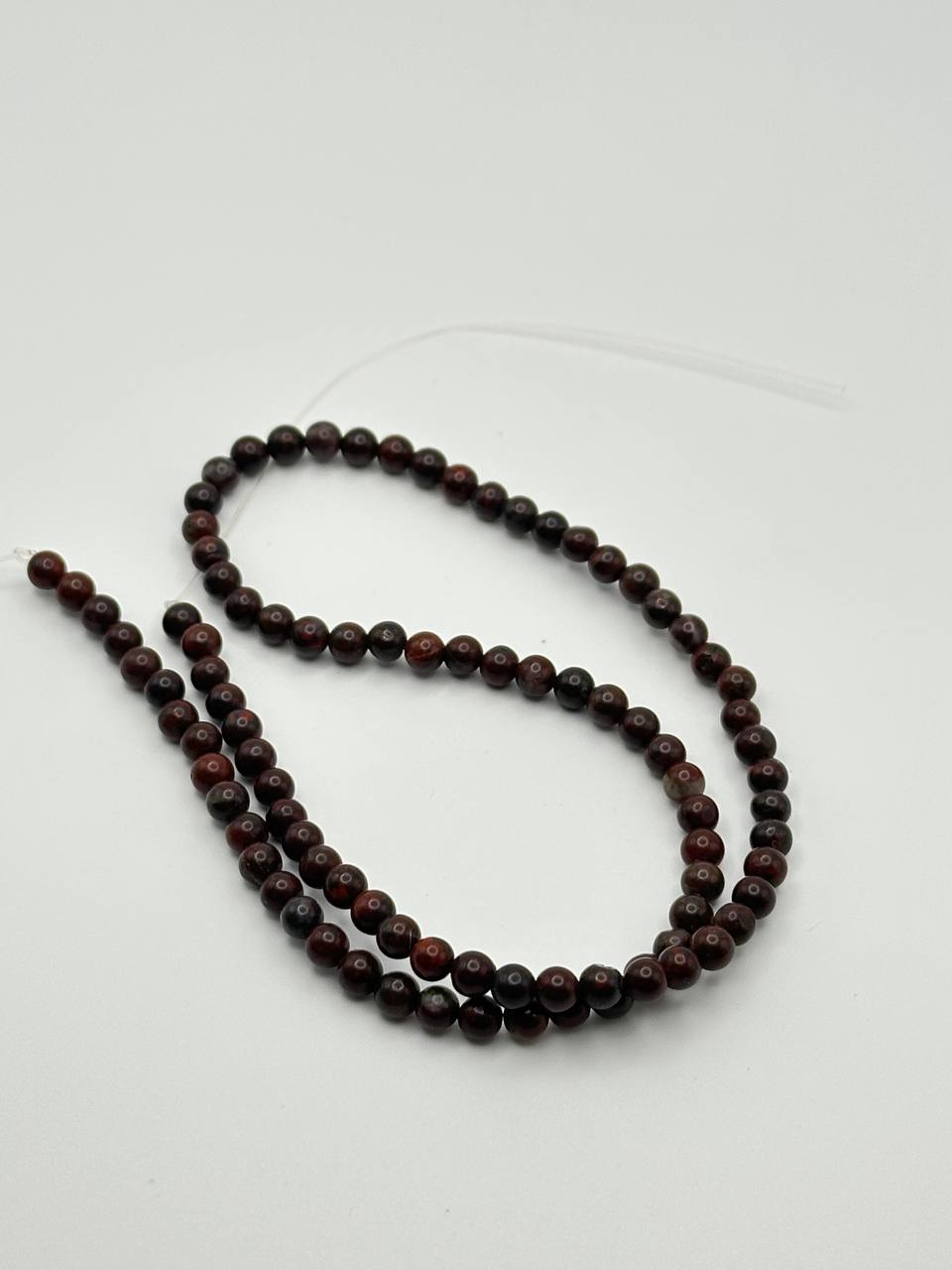 A string of dark red brecciated jasper round beads on a white surface