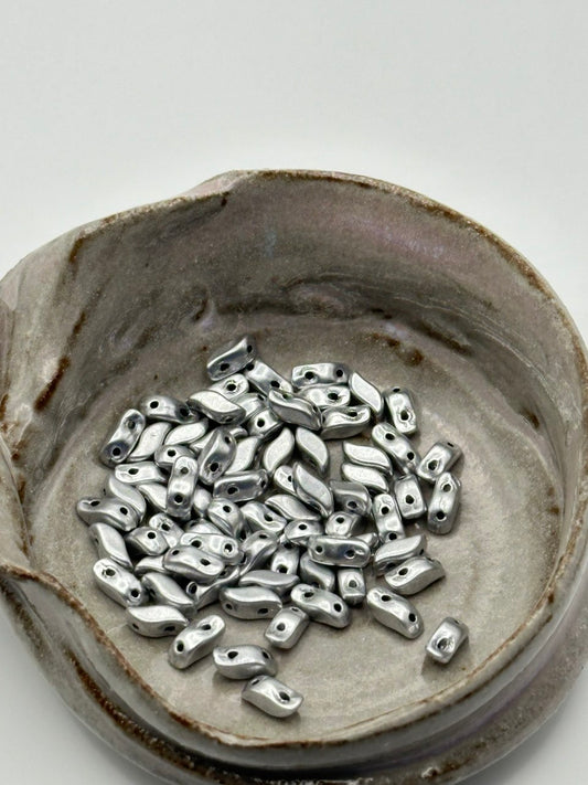 Silver beads in a ceramic dish on a white background