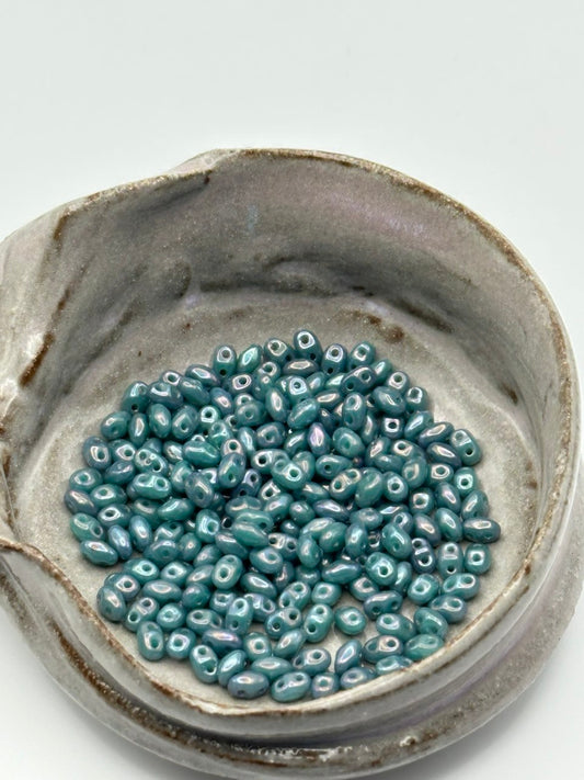 Small ceramic dish with miniduo nebula opaque turquoise beads on a light gray background