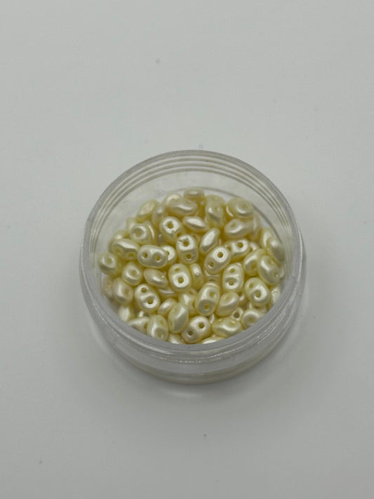 Small container filled with small light cream superduo beads on a light gray background