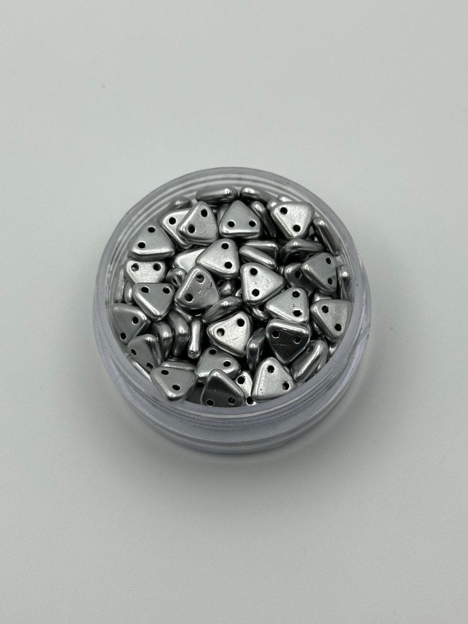 Jar of silver triangle beads on a light gray background