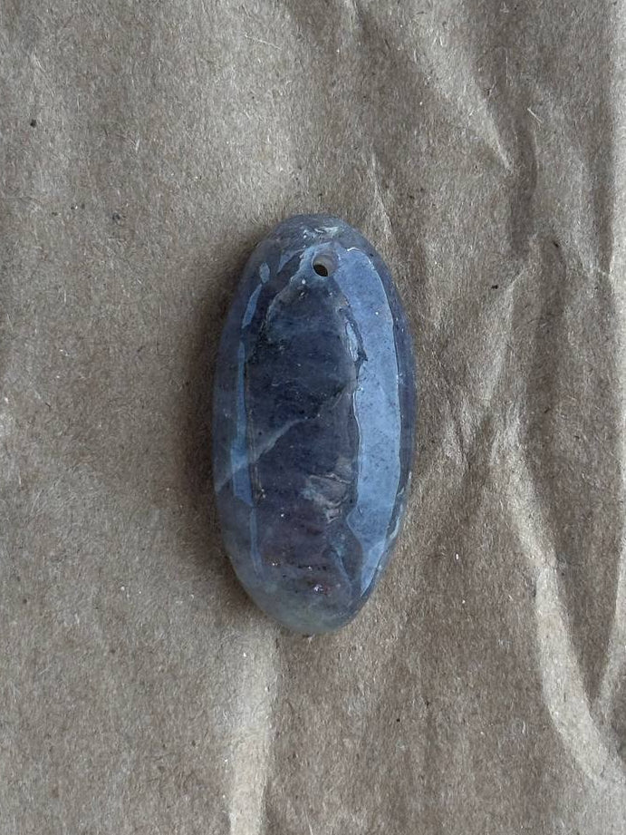 A small oval blue stone or cabochon with a rough carved center, placed on a wrinkled brown paper background.