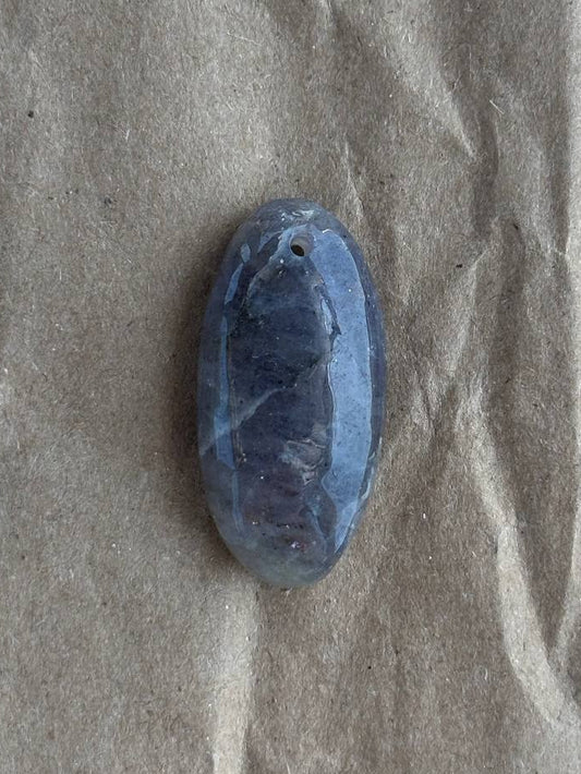 A small oval blue stone or cabochon with a rough carved center, placed on a wrinkled brown paper background.