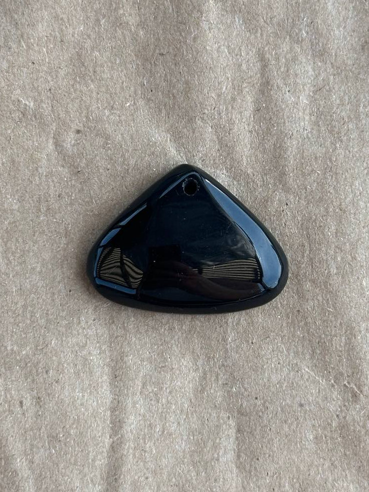 A glossy black triangular gemstone cabochon pendant with a small hole at the top, resting on a textured beige paper background.