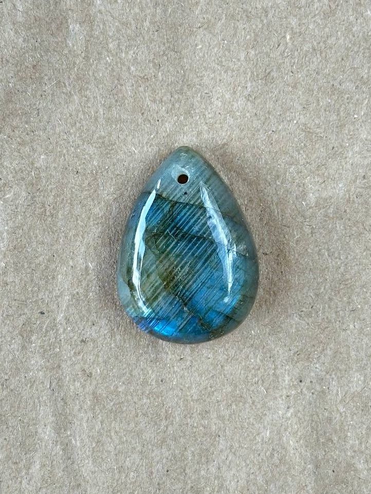 A small teardrop shaped labradorite stone on brown paper background