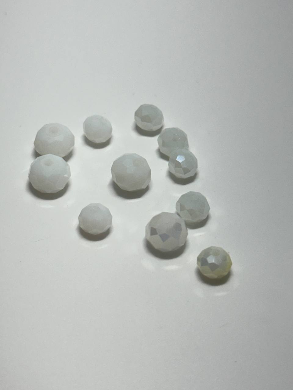 A group of small faceted glass beads in white and pale gray, arranged on a plain light background.