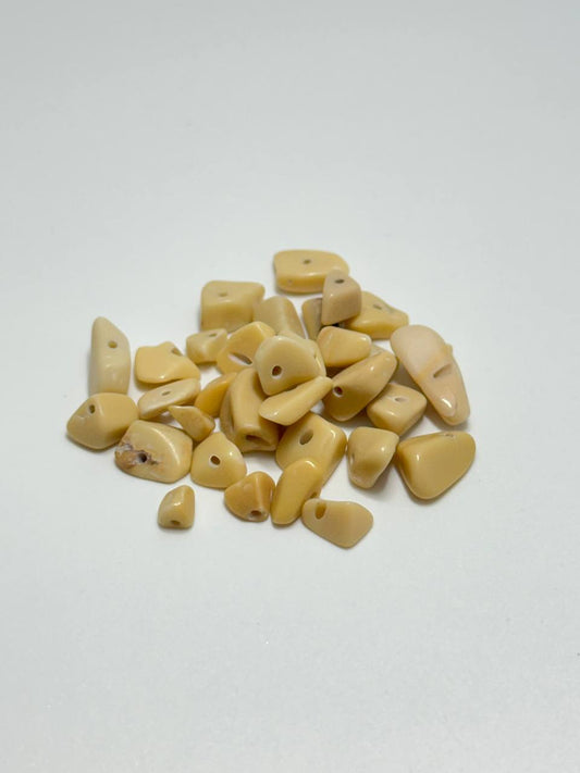 A pile of small, irregularly shaped cream-colored stone beads with drilled holes, arranged on a plain white surface.