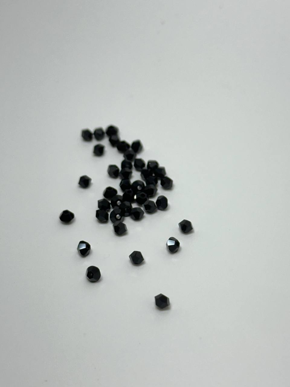 A small pile of tiny 3mm jet bicone beads on white surface
