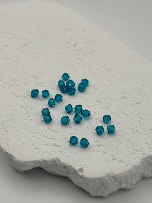 Blue zircon bicone beads on a textured white surface