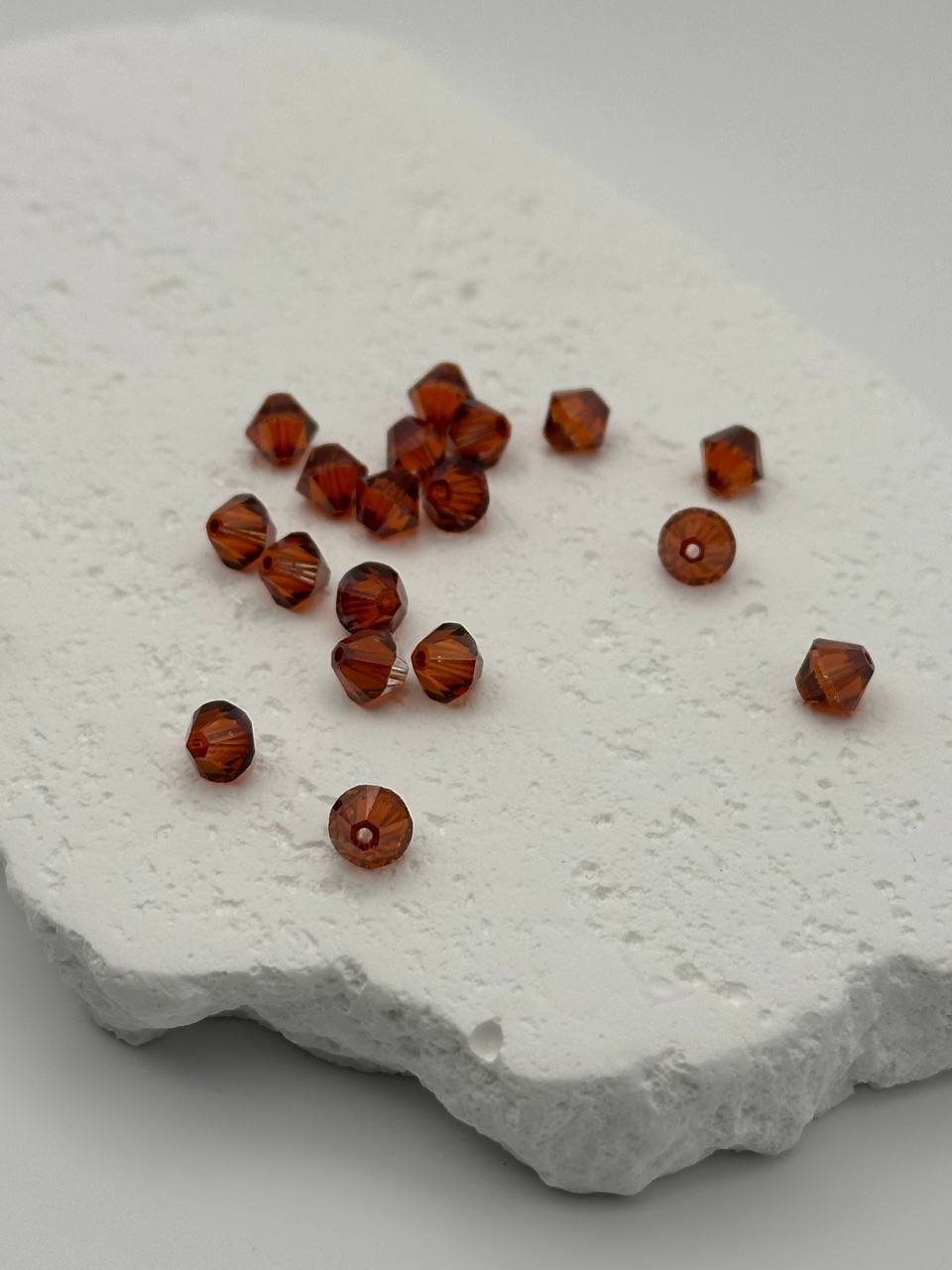 Smoked Topaz bicone beads on a textured white surface