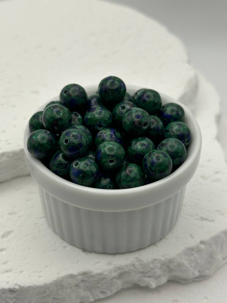 White ramekin filled with green beads on a textured white surface
