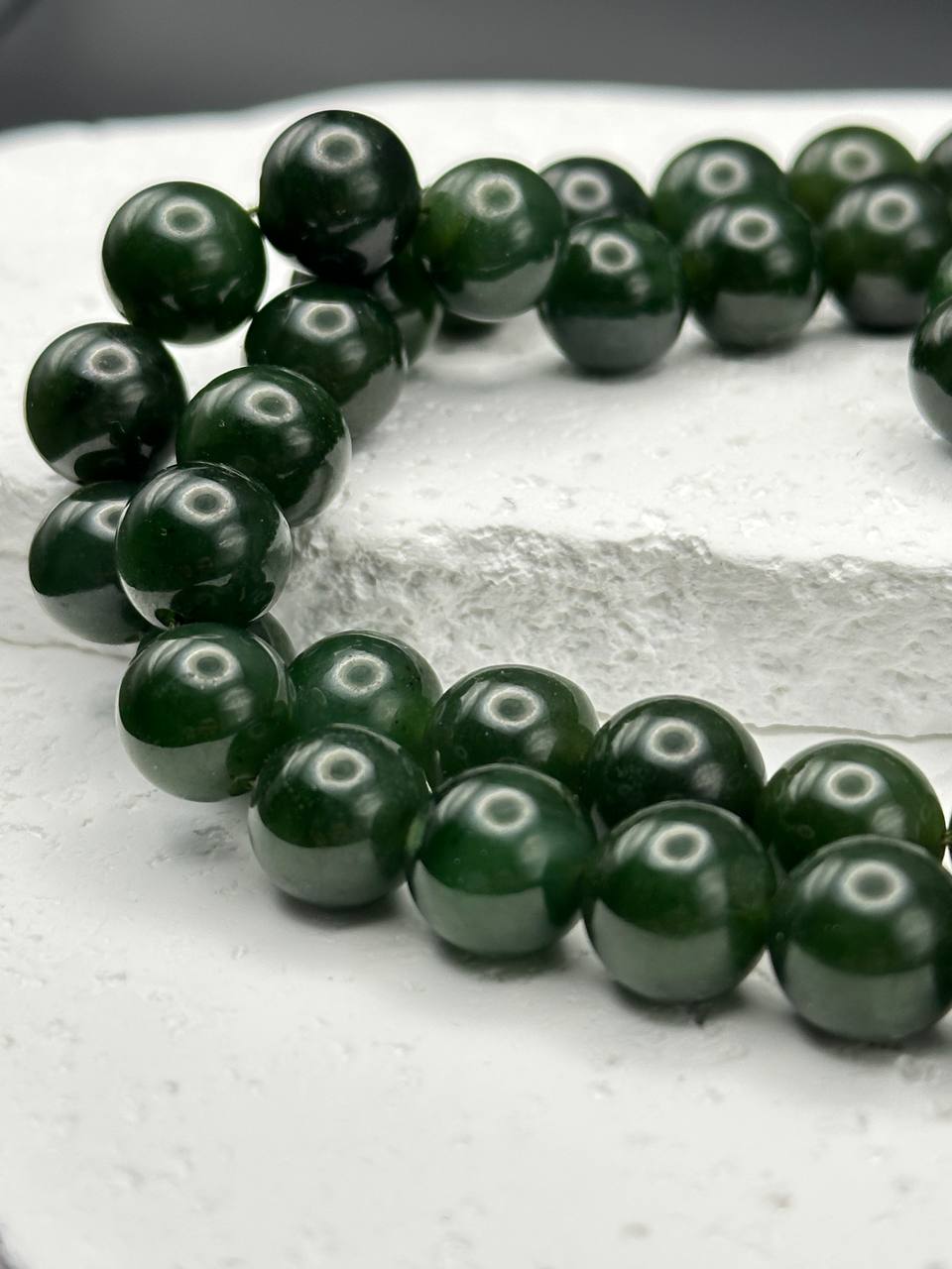 Necklace of dark green beads with white spots on a light gray surface