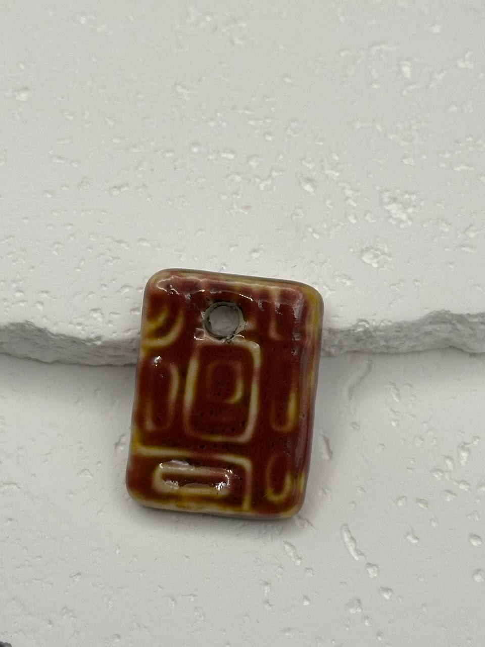 Rectangular ceramic pendant with brown and beige design on a white background