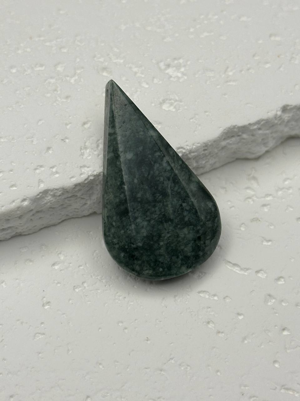 Green stone with a teardrop shape on a light gray surface