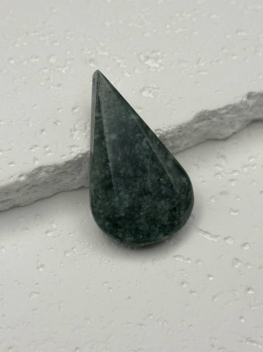 Green stone with a teardrop shape on a light gray surface