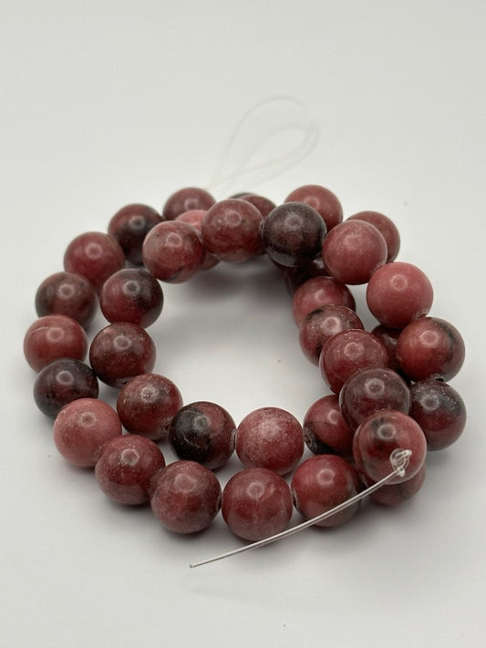 dark pink rhodonite beads on white surface