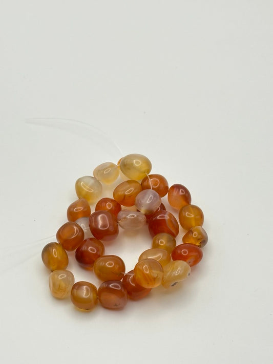 A string of red, orange, and yellow nugget carnelian agate beads on a white surface.