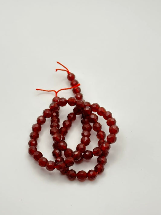 a string of red faceted carnelian agate beads on a white surface