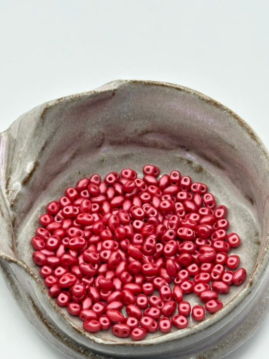 Small container filled with red miniduo beads on a light gray background