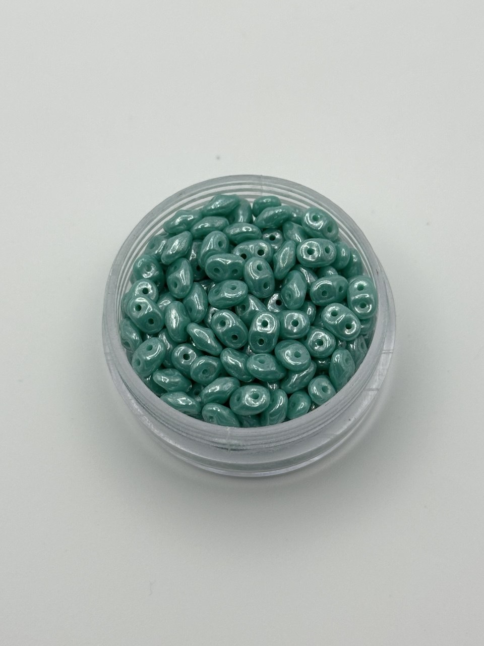 Jar of teal SuperDuo beads on a white background