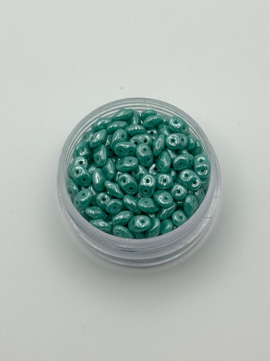 Jar of teal SuperDuo beads on a white background