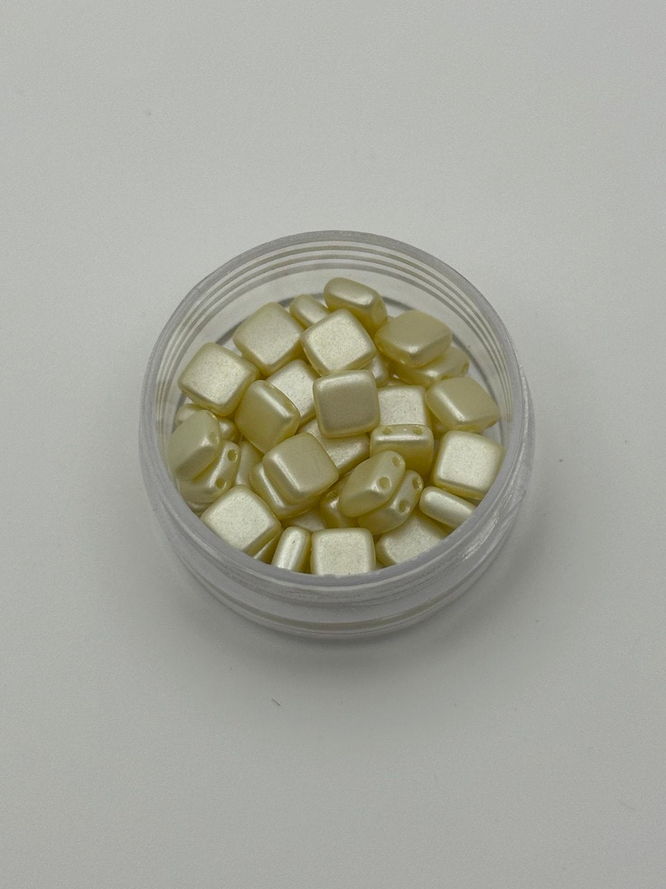 Clear container with small square 2 hole beads on a light gray background