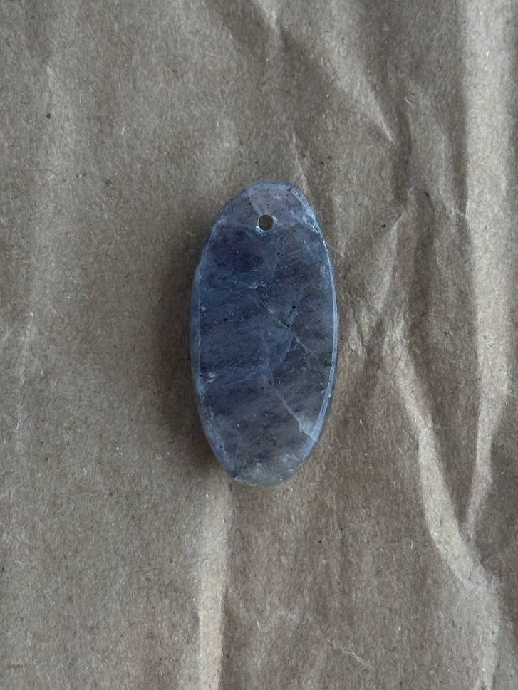 A polished oval blue stone pendant with a small hole at the top, resting on a textured brown paper background.