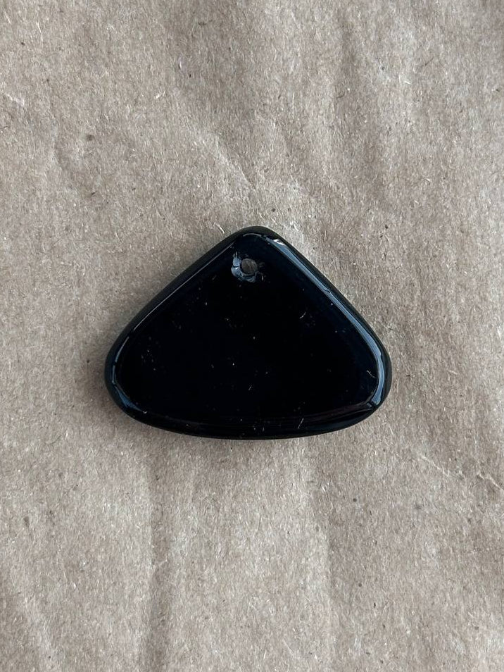 A small polished black triangular stone or cabochon with a rounded top, placed on a textured beige paper background.