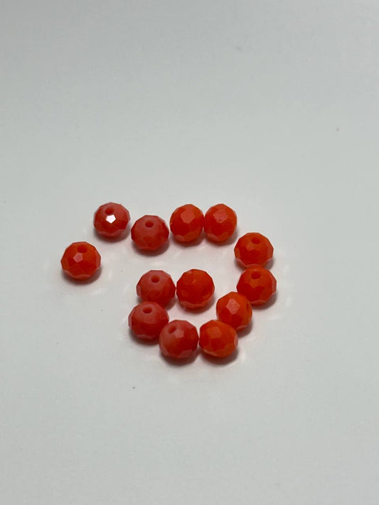 A group of faceted orange-red beads arranged in a loose spiral on a plain light gray background.