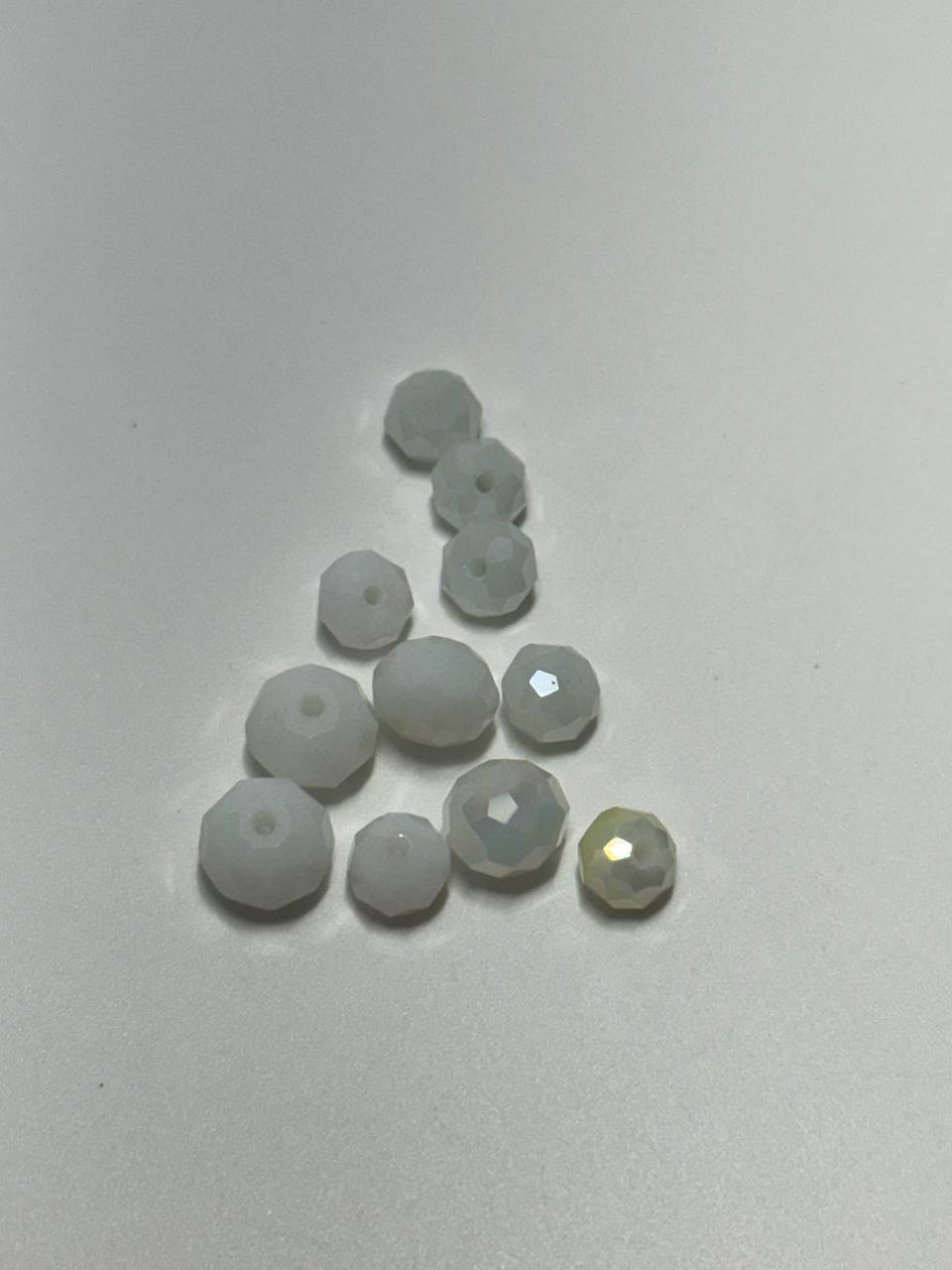 A group of small translucent white faceted beads arranged in a triangle on a plain light background, with one bead at the bottom right showing a pale gold iridescent reflection.