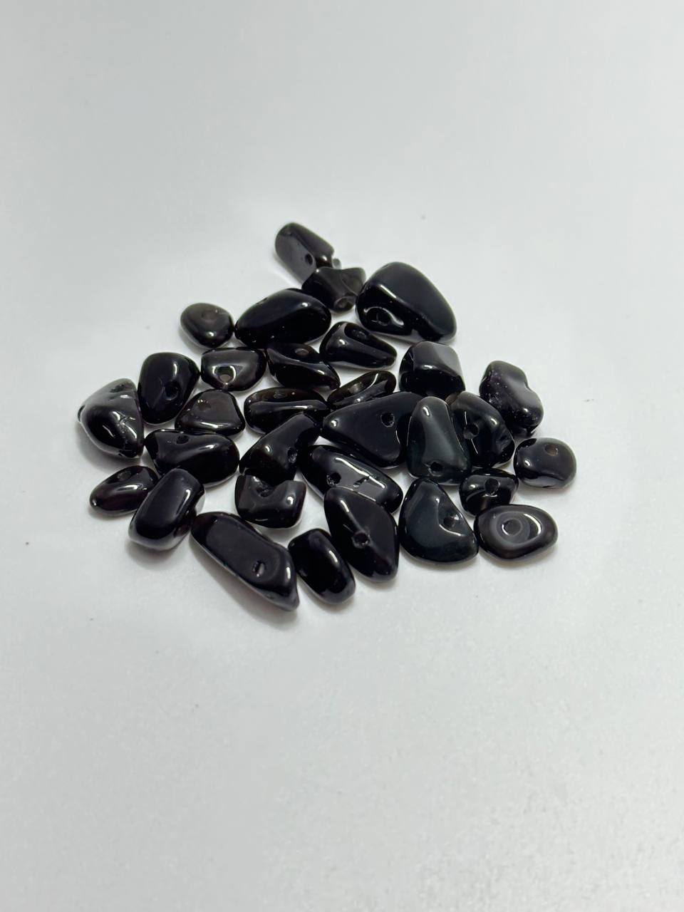 A pile of polished black tumbled agate stones, arranged on a plain white surface.