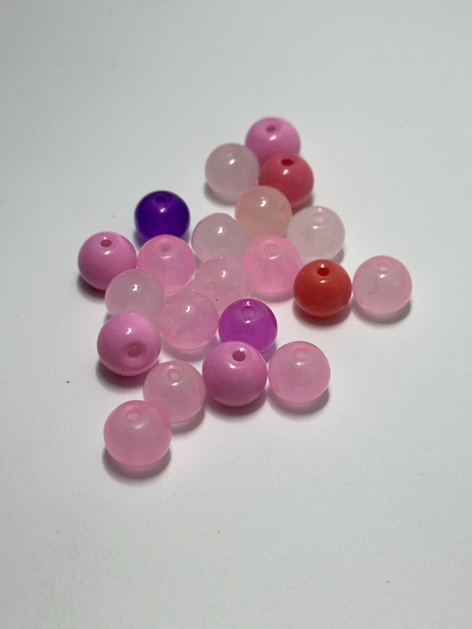 A small pile of round translucent beads in shades of pink, red, and purple on a plain light background.