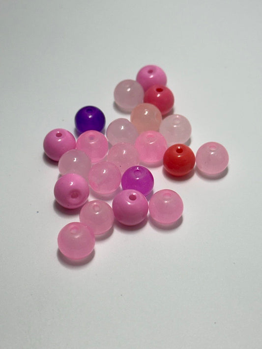 A small pile of round translucent beads in shades of pink, red, and purple on a plain light background.