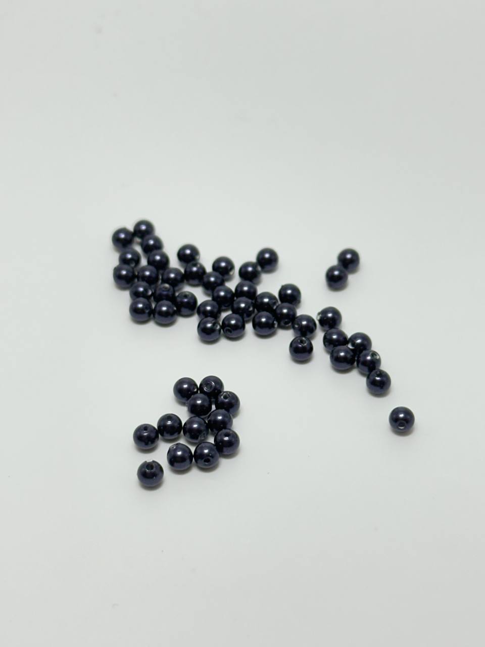 A group of small, glossy, dark blue-black round beads scattered on a plain white surface.