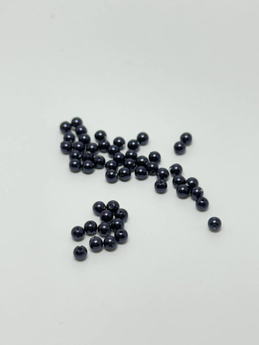 A group of small, glossy, dark blue-black round beads scattered on a plain white surface.
