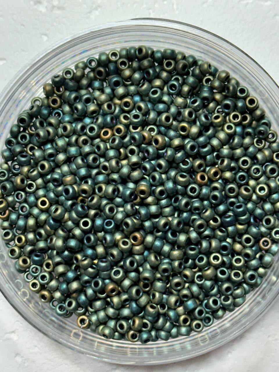a small pile of miyuki size 8 metallic patina iris matte seed beads on white surface