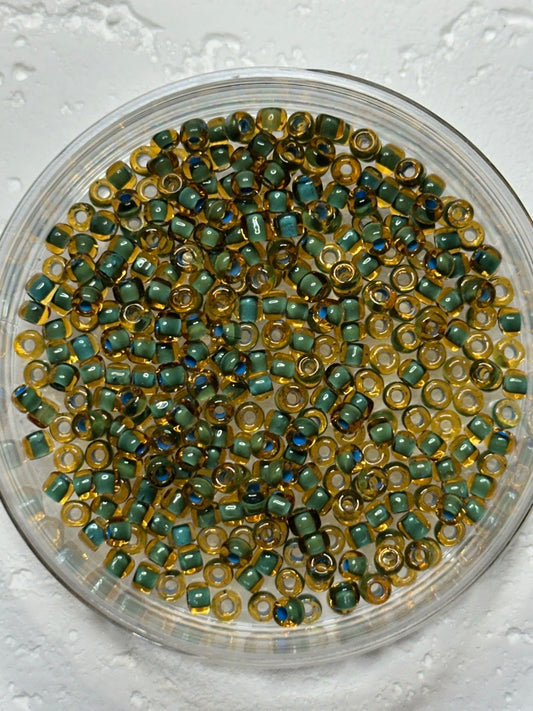 A small pile of toho size 6 in seafoam lined dark topaz seed beads on white surface