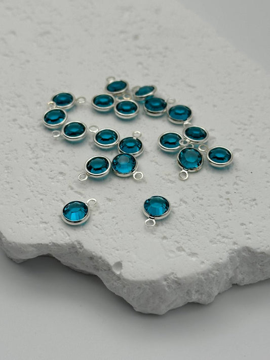 Silver jewelry components with blue crystals on a textured stone surface