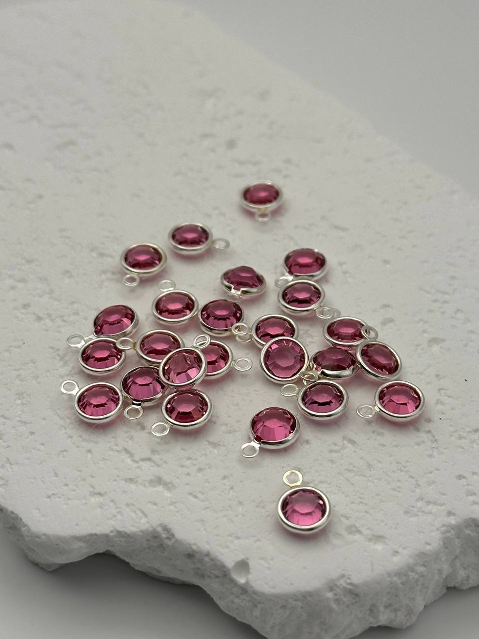 Silver jewelry components with pink chatons on a textured white surface
