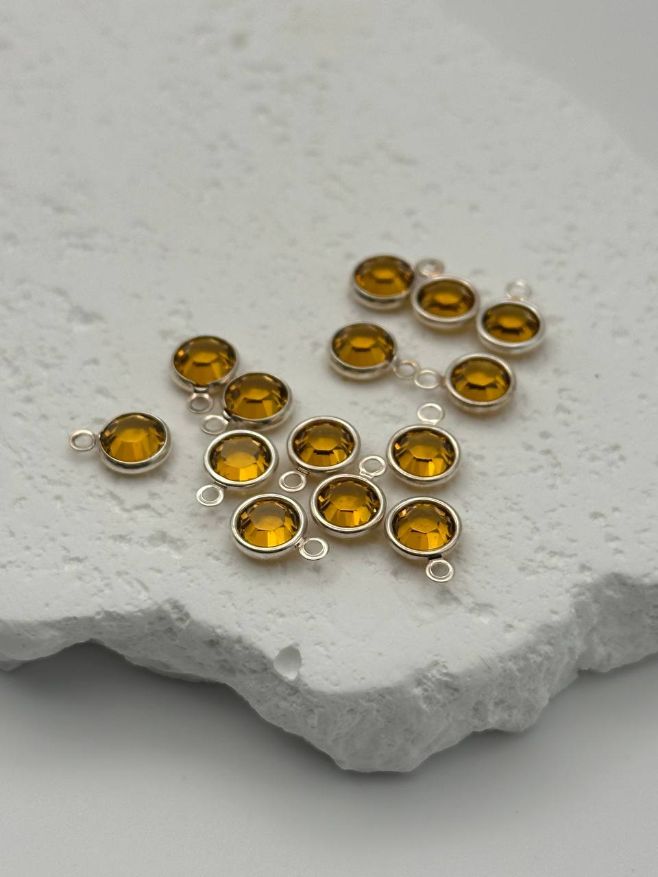 Silver jewelry piece with amber-colored chatons on a textured white surface