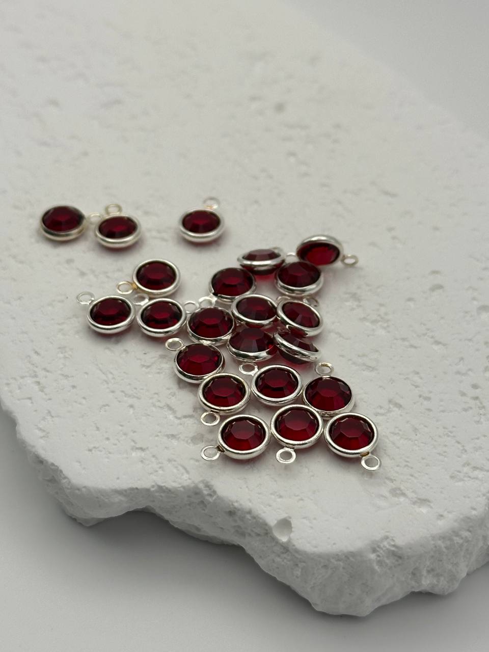 Silver pendants with red chatons on a textured white surface