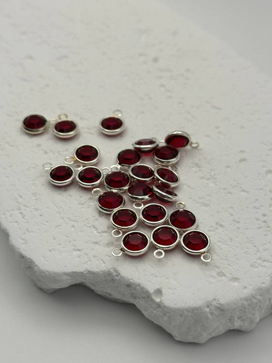 Silver pendants with red chatons on a textured white surface