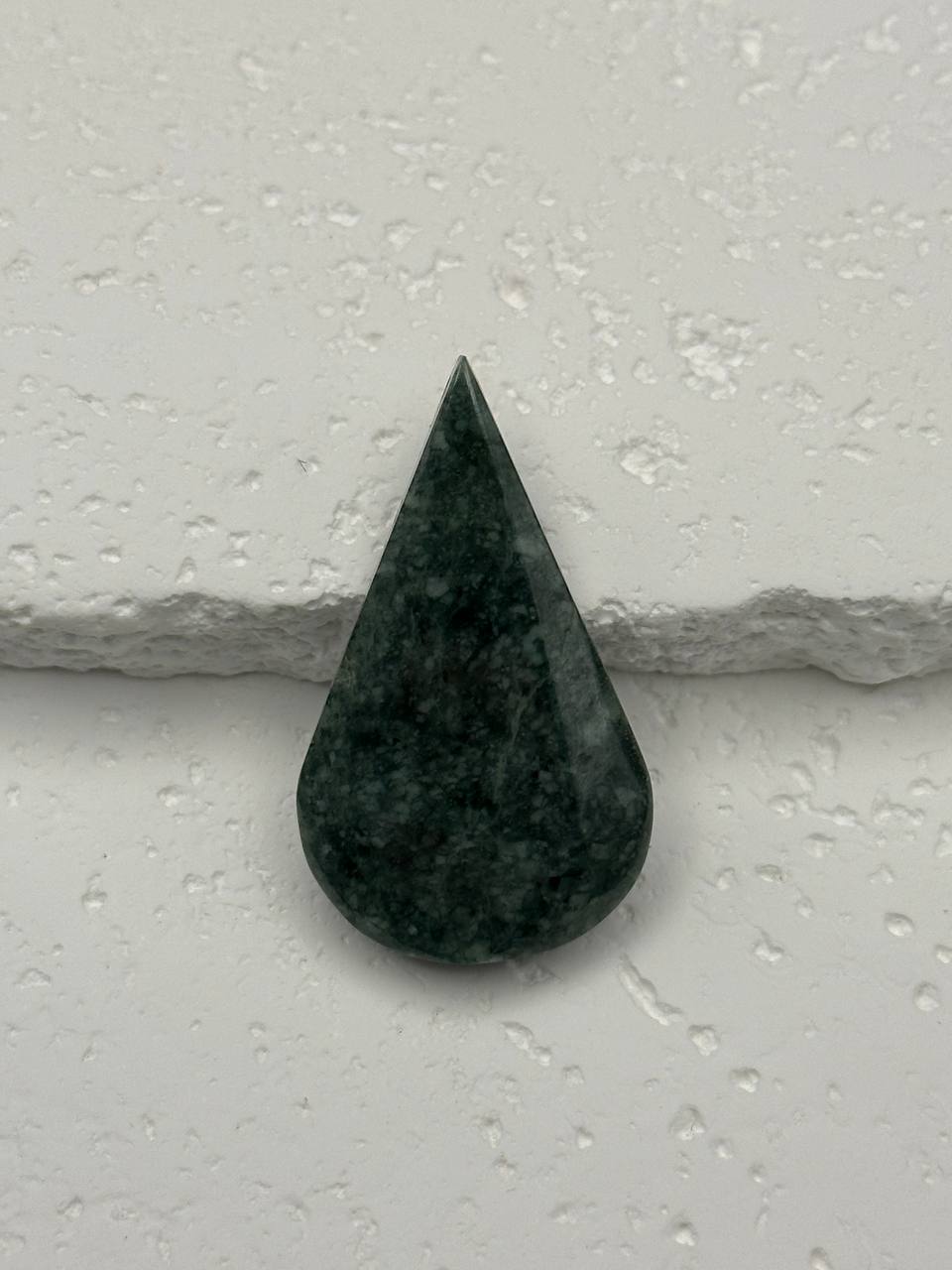 Teardrop-shaped green stone on a light gray surface