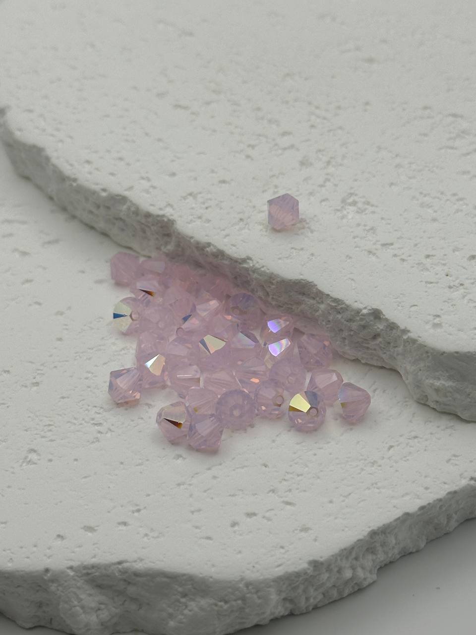 Pink crystal bicone beads on a textured gray surface