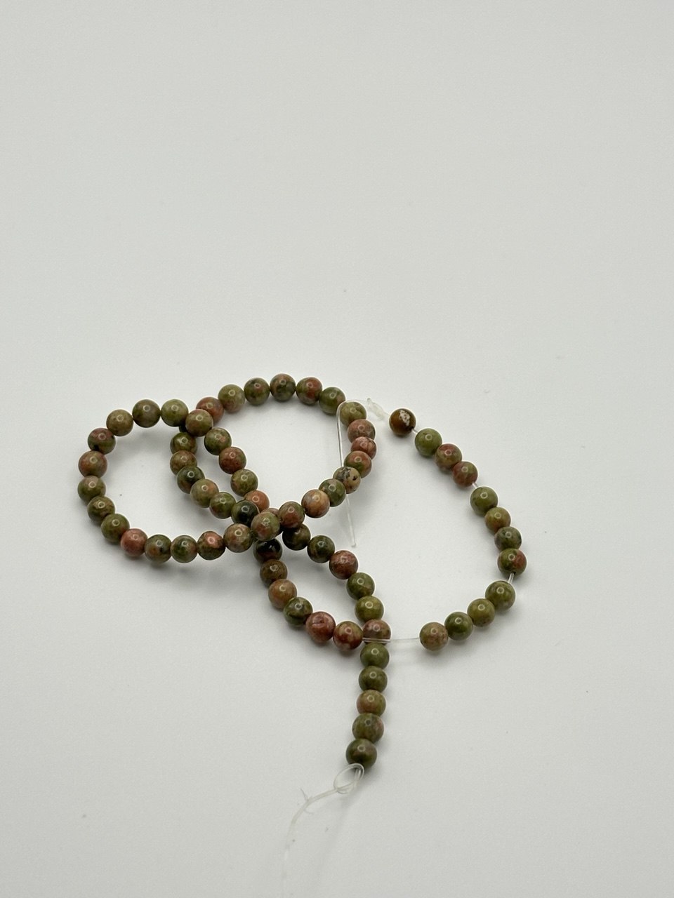 a string of green and red unakite round beads on a white surface