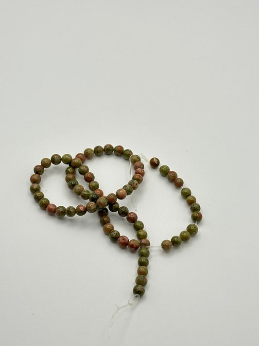 a string of green and red unakite round beads on a white surface