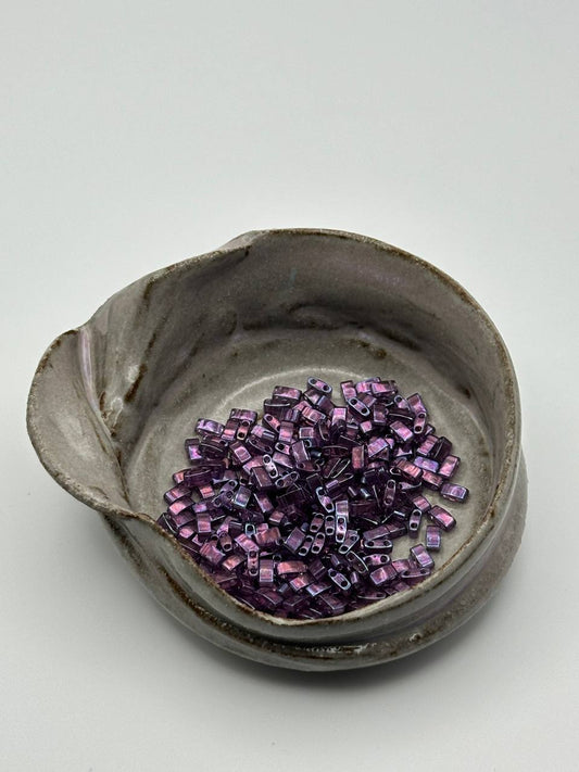 Small ceramic bowl with purple beads on a light gray background