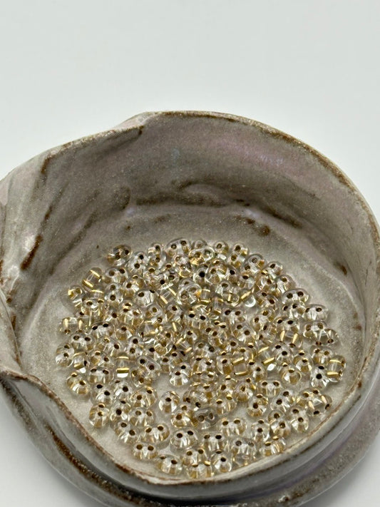 Small container filled with small twin 2-hole beads on a light gray background