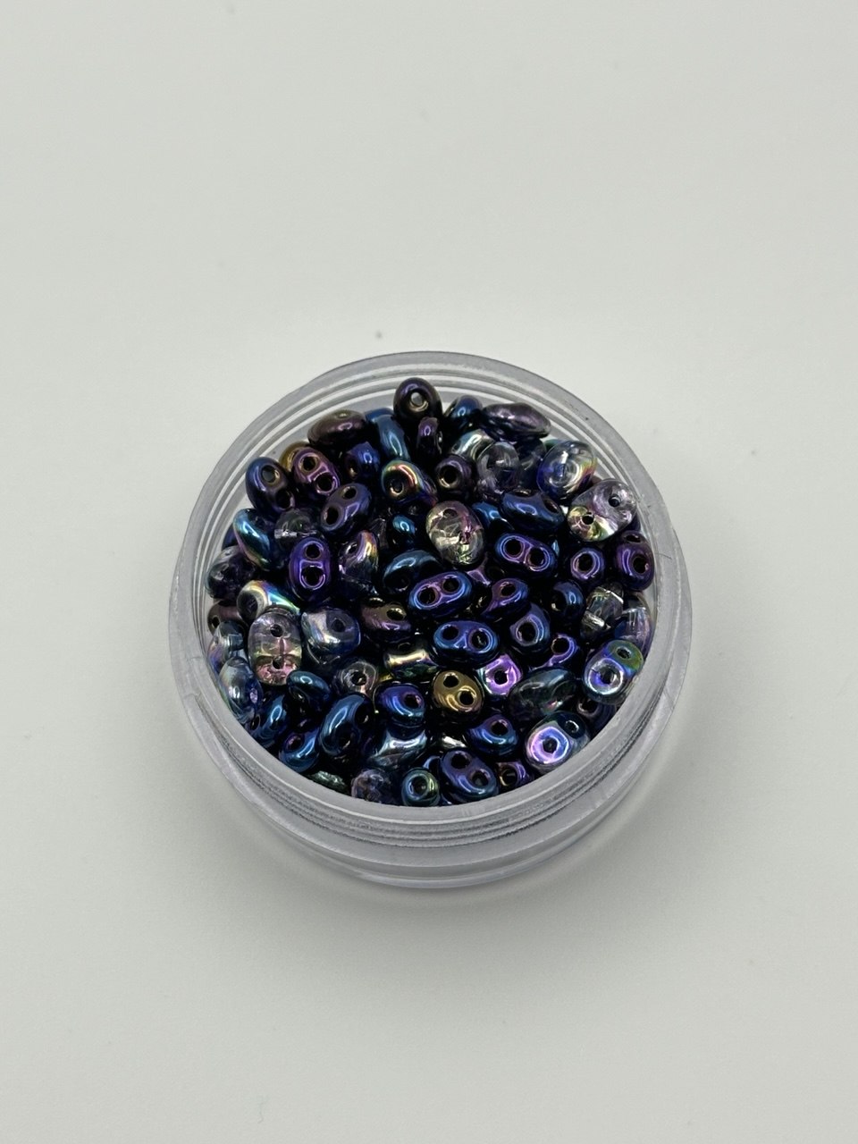 Jar of small, multicolored superduo beads on a white background